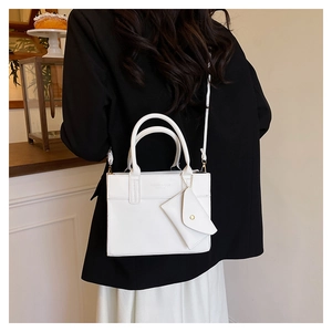 Detail view of a white leather handbag with a mini triangle pouch and round handles
