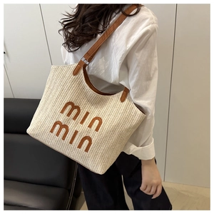 Detail of hand-woven straw tote with brown leather straps and embroidered min min text