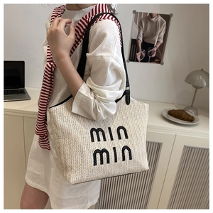 Detail of woven straw tote bag with black min min embroidery and contrast strap