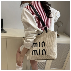 Detail of woven straw tote bag with black 'min min' embroidery and leather straps