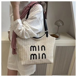 Detail of woven straw tote bag with black min min embroidery and leather straps