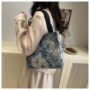 Detail of blue floral jacquard tote bag with black canvas strap in a cozy home setting