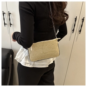 Détail d'un sac bandoulière en paille beige avec perles foncées et chaîne argentée sur modèle