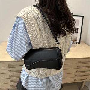 Minimalist black underarm bag with curved flap and gold hardware in a cozy indoor setting