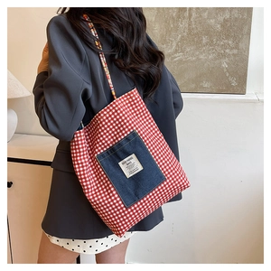 Detail of red plaid tote bag featuring a denim front pocket and woven colorful straps