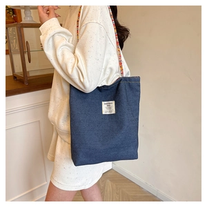 Detail view of denim tote bag featuring a colorful woven strap and front logo patch