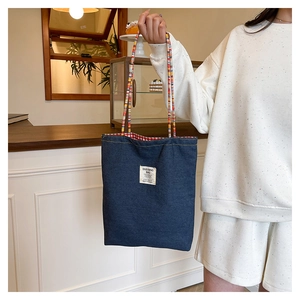 Detail of blue denim tote bag with colorful patterned straps and internal red gingham lining