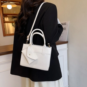Minimalist white tote bag with gold hardware and envelope charm shown in a modern interior