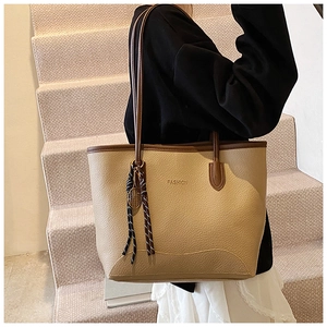 Detail of beige tote bag with litchi texture and brown straps on a model's shoulder