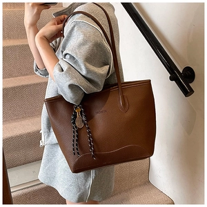 Detail of a brown leather tote bag with FASHION embossing and a tennis racket charm