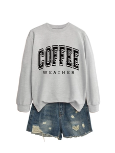 Flat lay of a grey crewneck sweatshirt with Coffee Weather print and ripped denim shorts