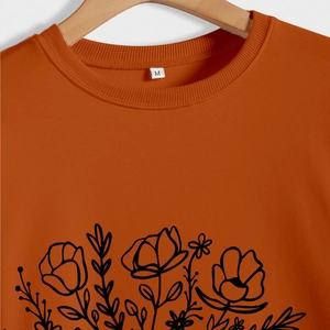Détail du col d'un sweat-shirt orange avec motif floral imprimé et étiquette de taille M