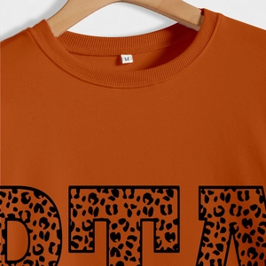 Détail du col côtelé du sweat orange brûlé avec étiquette M et texte léopard