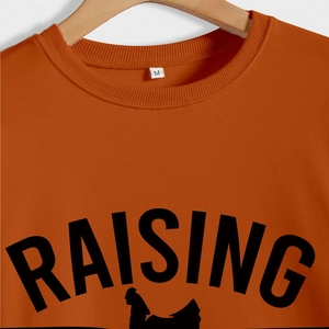 Détail du sweat col rond orange brûlé avec texte Raising et silhouette de coq noir