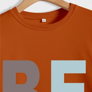 Détail du col côtelé et de l'imprimé graphique sur un sweat-shirt col rond caramel