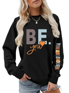 Détail de l'imprimé 'YOU ARE ENOUGH' sur la manche d'un sweat noir à col rond