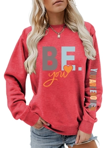 Détail d'un sweat rouge à col rond avec graphique BE YOU et texte sur la manche
