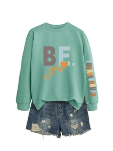 Détail d'un sweat vert menthe avec imprimé et d'un short en jean bleu à effet déchiré