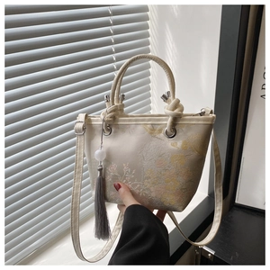 Detailed embroidery of floral patterns and silk tassel on a cream crossbody bucket bag