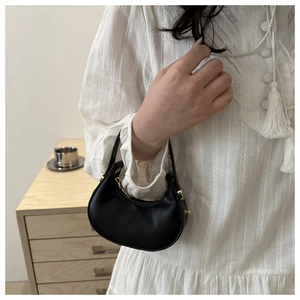 Détail du sac demi-lune en cuir noir avec ferrures dorées tenu par un mannequin en dentelle