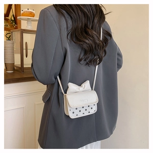 Mini sac bandoulière crème à pois noirs avec nœud en cuir, porté par un mannequin en intérieur