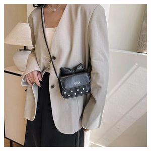 Detail of a black leather crossbody bag with a 3D bow and white polka dot design on a model