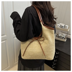 Detailed view of beige straw tote bag featuring a leather bow and brown shoulder straps