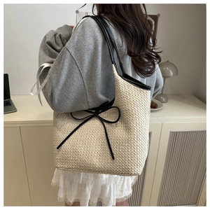 Close-up of woven straw tote bag with black leather straps and decorative bow detail