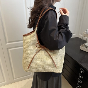 Large straw tote bag with brown leather trim and bow detail shown on a model