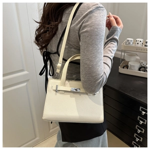 Detail of off-white lychee pattern leather handbag with metal buckle on a woman