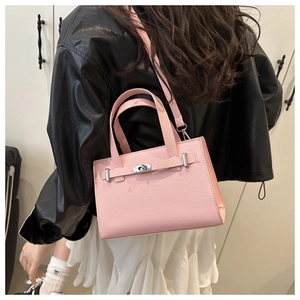 Close-up of a pink pebbled leather tote bag with silver lock worn by a model in street style