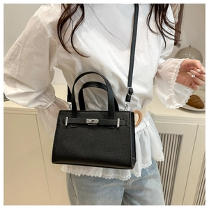 Detail of black lychee grain leather handbag with silver lock and adjustable strap
