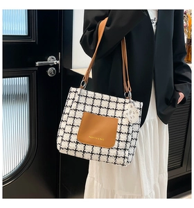 Detail of houndstooth tote bag featuring a brown leather pocket and cute cat charm