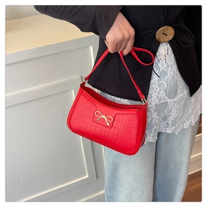 Detail of red crocodile pattern shoulder bag with a gold bow metal accent on front