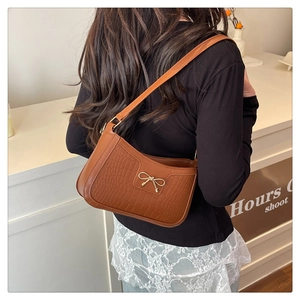 Sac à bandoulière marron à motif crocodile et nœud doré porté par un mannequin de dos