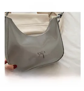 Detailed close-up of glossy patent leather baguette bag with metal bow buckle and zipper