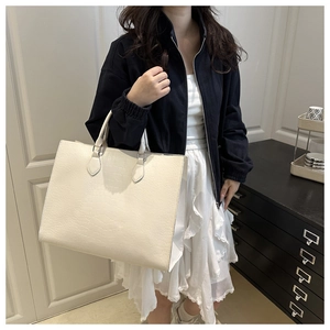 Detail of cream white tote bag with crocodile embossing worn by a model in casual style
