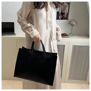 Detail of black crocodile pattern tote bag shown by model in a cozy office setting