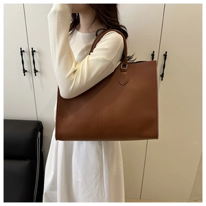 Detail shot of a brown large-capacity tote bag with crocodile pattern worn by a model