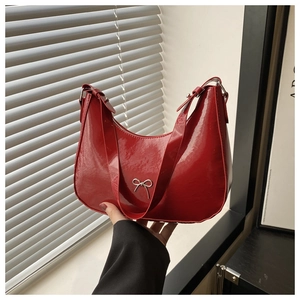 Close-up of bright red patent leather handbag featuring a silver metal bow detail