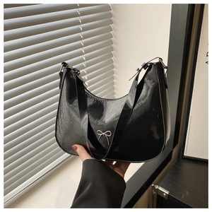 Detail of glossy black patent leather shoulder bag with silver bow accent