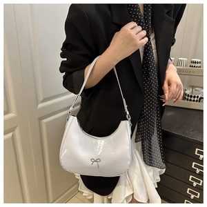Detail shot of white patent leather hobo bag with a silver bow and sleek shoulder strap