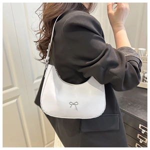 Detail of white crescent shoulder bag with glossy finish and silver bow charm accent