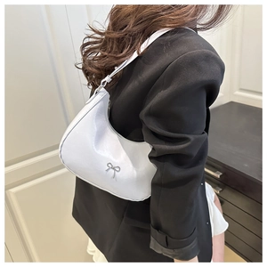 Detail view of a glossy light grey hobo bag with metal bow on a model's shoulder