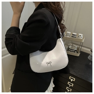 Detail of white glossy leather underarm bag with silver bow accent on model shoulder