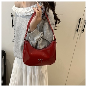 Close-up of red patent leather underarm bag featuring a silver metal bow accent