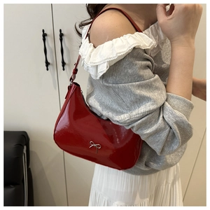 Detail of red patent leather underarm bag with silver metal bow and crescent hobo design
