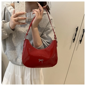 Close-up of red patent leather underarm bag featuring a silver bow accent and glossy finish