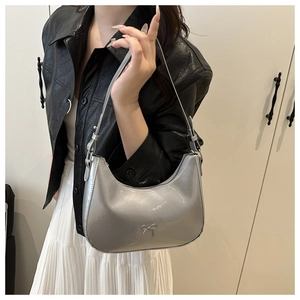 Close-up of metallic silver underarm bag featuring a small metal bow and adjustable strap