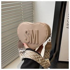 Detail of beige heart-shaped crossbody bag with embossed SM logo and woven strap